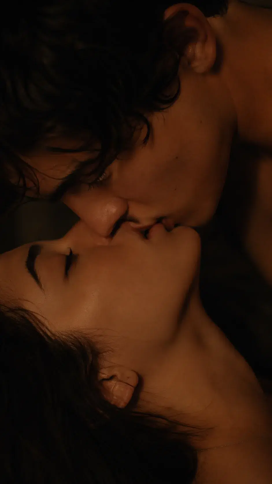 Cinematic close-up of an adult couple sharing a tender kiss in warm light
